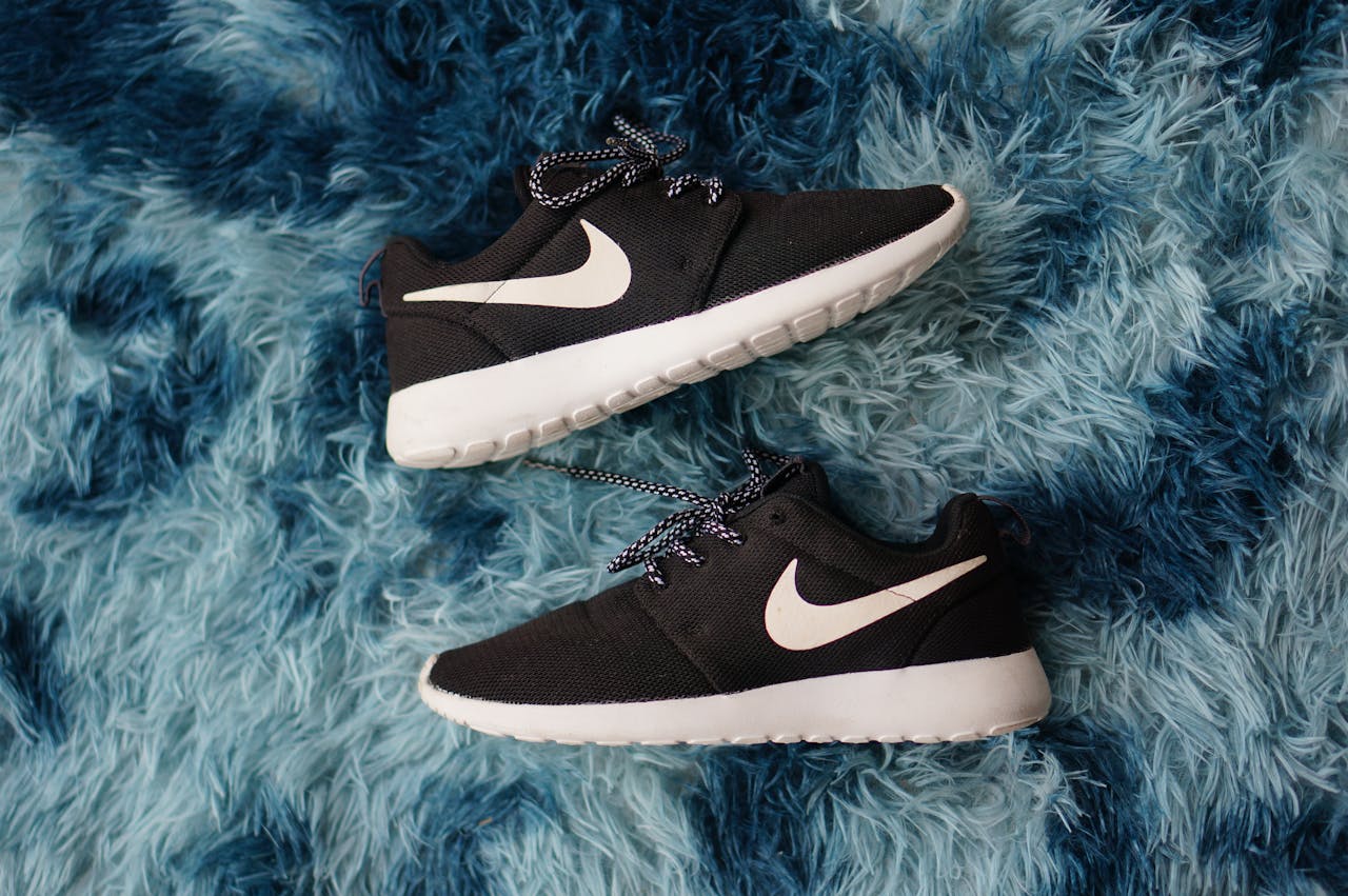 Top view of black sneakers on textured blue fluffy rug, showing stylish footwear design.